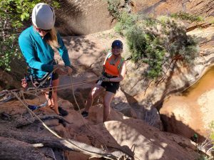 Professional guide managing ropes for a client rappelling down a sandstone cliff in Water Canyon, Utah.