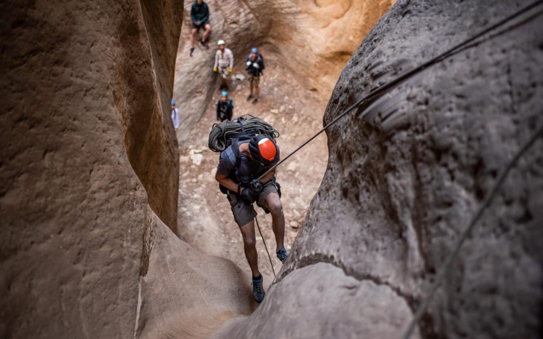 Canyoneer rappelling down a narrow sandstone slot canyon during a guided adventure in East Zion.